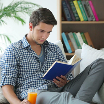 a man reading a book while relaxing and holding orange juice
